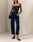 A model wearing a softly sculpted barrel leg jean with silver rivet details, a dark brown strapless top, and black high-heeled mules, standing in a minimalist beige studio corner.

Le Jean Delphine Jean in Midnight Rodeo. Available at Edit by Elaine Turner in Houston, TX. Full model close-up view. 