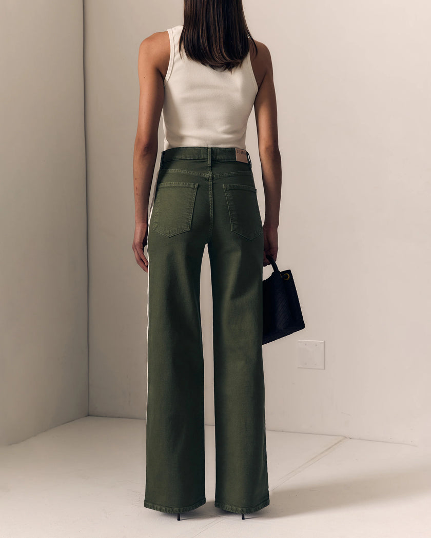 A model shown from the back wearing olive green wide-leg pants with a white ribbed tank top and holding a black handbag, set against a minimalist beige studio background.

Le Jean Track Column Jeans in Olive Green. Available at Edit by Elaine Turner in Houston, TX. Full Model Back View. 