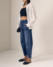 A model wearing a pair of relaxed, wide straight leg blue jeans with a black crop top, white button-up shirt, and black studded flats, standing in a minimalist studio setting.

Le Jean Utility Soft Barrel in London Calling. Available at Edit by Elaine Turner in Houston, TX. Full model side view. 