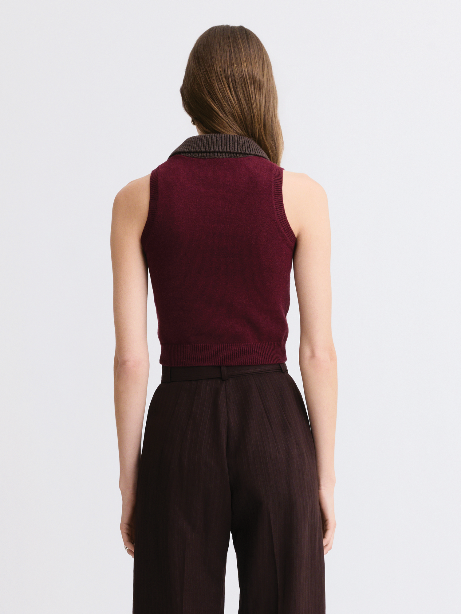A woman shown from the back wearing a sleeveless burgundy knit top with a dark ribbed collar and dark brown wide-leg trousers, against a light gray studio background.

Matthew Bruch- Combo Collar Cropped Tank Top - Merlot Knit. Available at Edit by Elaine Turner in Houston, TX. Back Model View. 