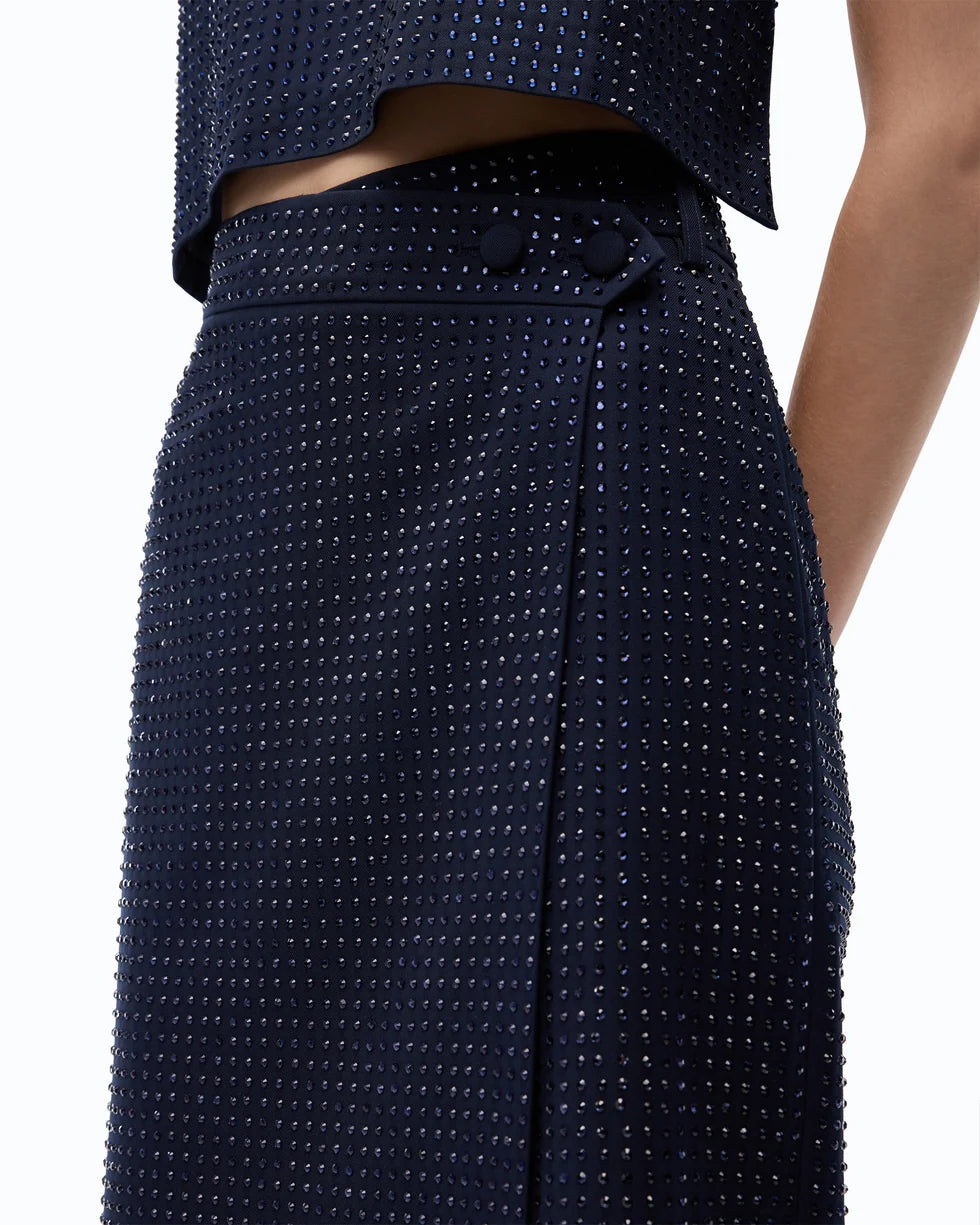 Close-up of a model wearing a dark navy blue textured skirt with a dotted studded pattern and a matching cropped top against a white background.

PINKO- Fully Rhinestoned Calf-Length Wrap Skirt in Iris Blue. Available at Edit by Elaine Turner in Houston, TX. Model Close Up view. 