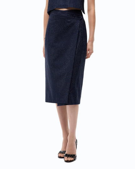 A model wearing a dark navy blue textured knit wrap midi skirt with a subtle dotted pattern, paired with black studded heels against a plain white background.

PINKO- Fully Rhinestoned Calf-Length Wrap Skirt in Iris Blue. Available at Edit by Elaine Turner in Houston, TX. Model Skirt view. 