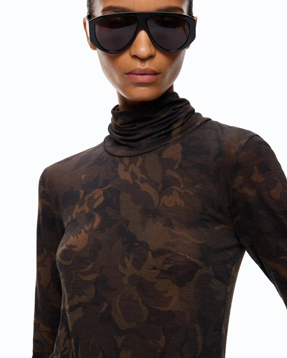 A close-up of a model wearing a sheer, long-sleeve turtleneck top with a dark brown and black floral camouflage pattern, paired with oversized black sunglasses, against a plain white background.

PINKO- Turtleneck Sweater with Floral Camouflage Print in Green & Black Multicolor. Available at Edit by Elaine Turner in Houston, TX. Close up model view. 