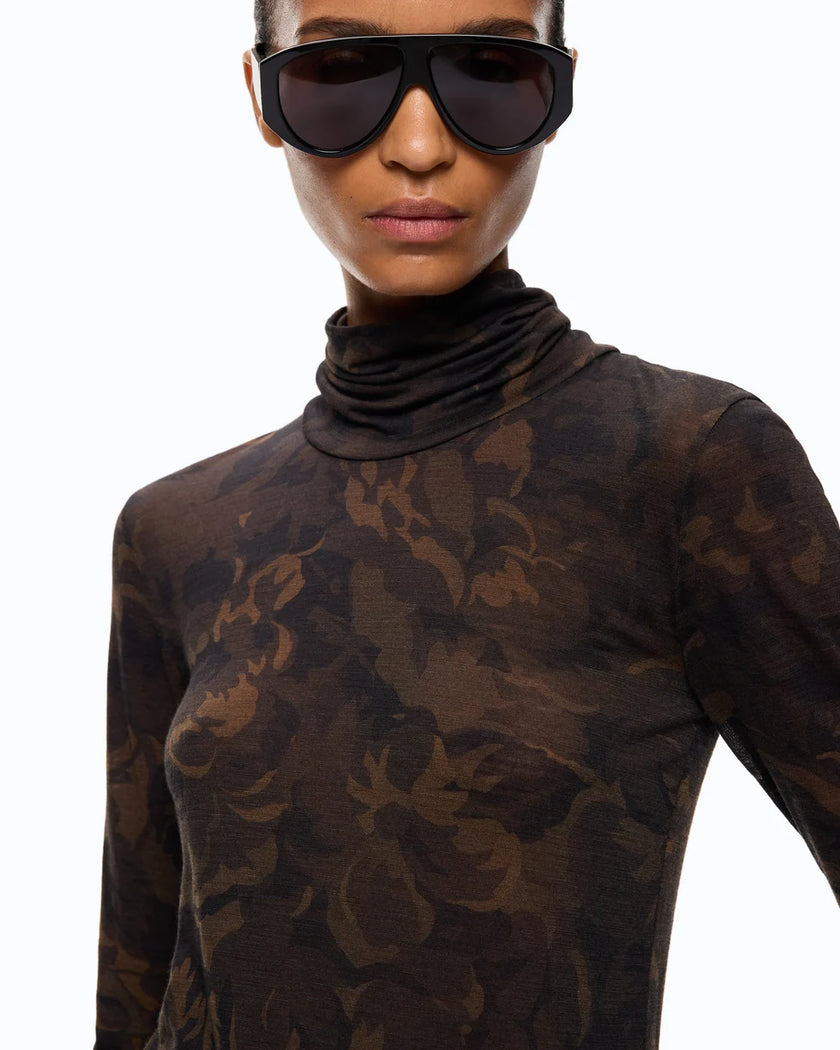 A close-up of a model wearing a sheer, long-sleeve turtleneck top with a dark brown and black floral camouflage pattern, paired with oversized black sunglasses, against a plain white background.

PINKO- Turtleneck Sweater with Floral Camouflage Print in Green & Black Multicolor. Available at Edit by Elaine Turner in Houston, TX. Close up model view. 