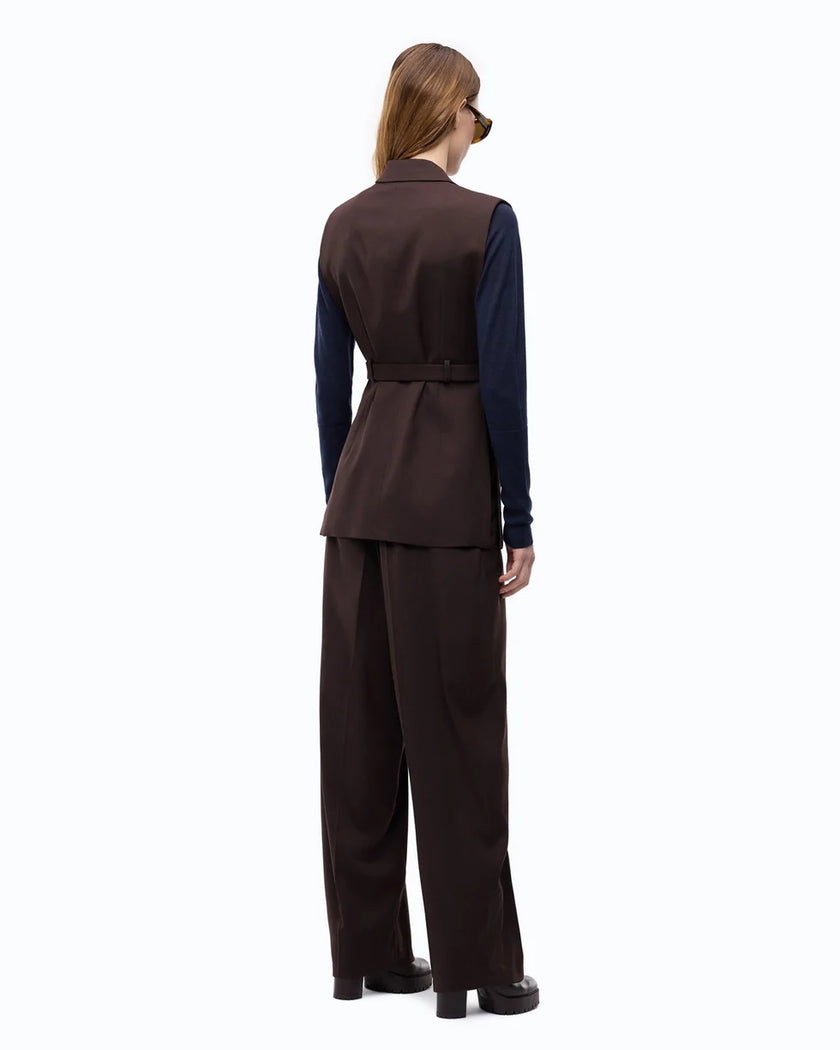 A model shown from the back wearing a dark brown tailored vest and matching wide-leg trousers over a navy blue long-sleeve top, photographed against a plain white studio background.

PIINKO- Vest with Open Sides and Belt in Beyond the Dark Brown. Available at Edit by Elaine Turner in Houston, TX. Full back model view. 