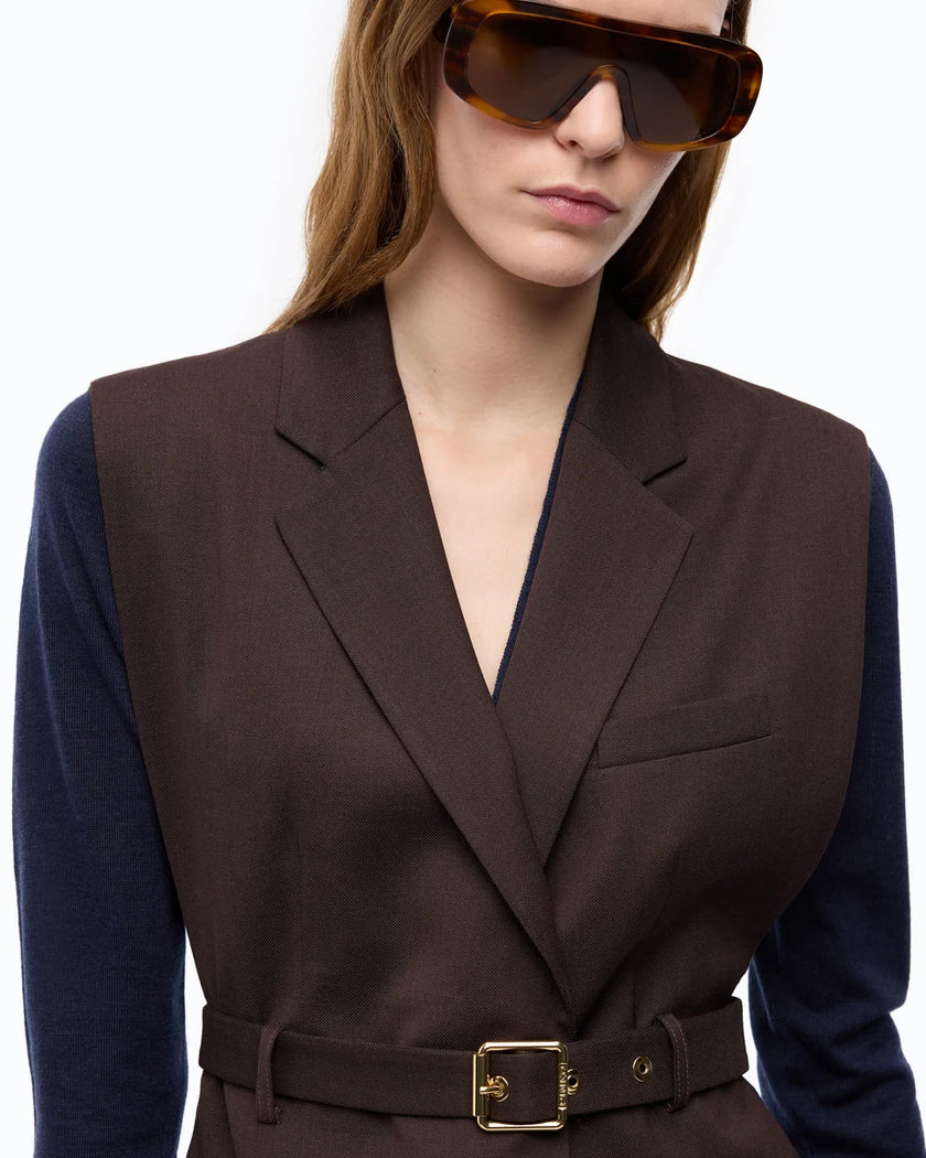 A close-up of a model wearing a dark brown tailored vest over a navy blue long-sleeve top, accessorized with oversized tortoiseshell sunglasses against a plain white background.

PIINKO- Vest with Open Sides and Belt in Beyond the Dark Brown. Available at Edit by Elaine Turner in Houston, TX. Front Model Close Up View. 