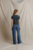 A woman stands with her back to the camera wearing a dark navy short-sleeve t-shirt and blue wide-leg jeans, posed in front of a draped beige fabric backdrop.

Perfect White Tee - Alanis in Turbulence. Available at Edit by Elaine Turner in Houston, TX. Model back view. 