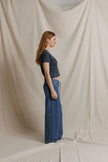 A woman stands in profile wearing a dark charcoal gray short-sleeve crop top and wide-leg blue jeans, posed against a draped beige fabric backdrop.

Perfect White Tee - Alanis in Turbulence. Available at Edit by Elaine Turner in Houston, TX. Model side view. 