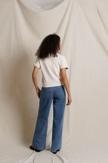 A model viewed from behind wearing blue wide-leg jeans and a cream colored top, standing against a draped cream fabric backdrop.

PerfectWhiteTee- Cleo French Terry short sleeve in Sugar. Available at Edit by Elaine Turner in Houston, TX. Full Model Back View. 