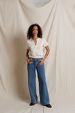 A woman stands against a draped cream fabric backdrop wearing a cream colored short-sleeve henley-style top with a split neckline and blue wide-leg jeans.

PerfectWhiteTee- Cleo French Terry short sleeve in Sugar. Available at Edit by Elaine Turner in Houston, TX. Full Model Front View. 