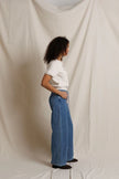 A woman stands in profile wearing a cream colored short-sleeve top and high-waisted, wide-leg blue denim jeans against a draped off-white fabric backdrop.

PerfectWhiteTee- Cleo French Terry short sleeve in Sugar. Available at Edit by Elaine Turner in Houston, TX. Full Model Side View. 