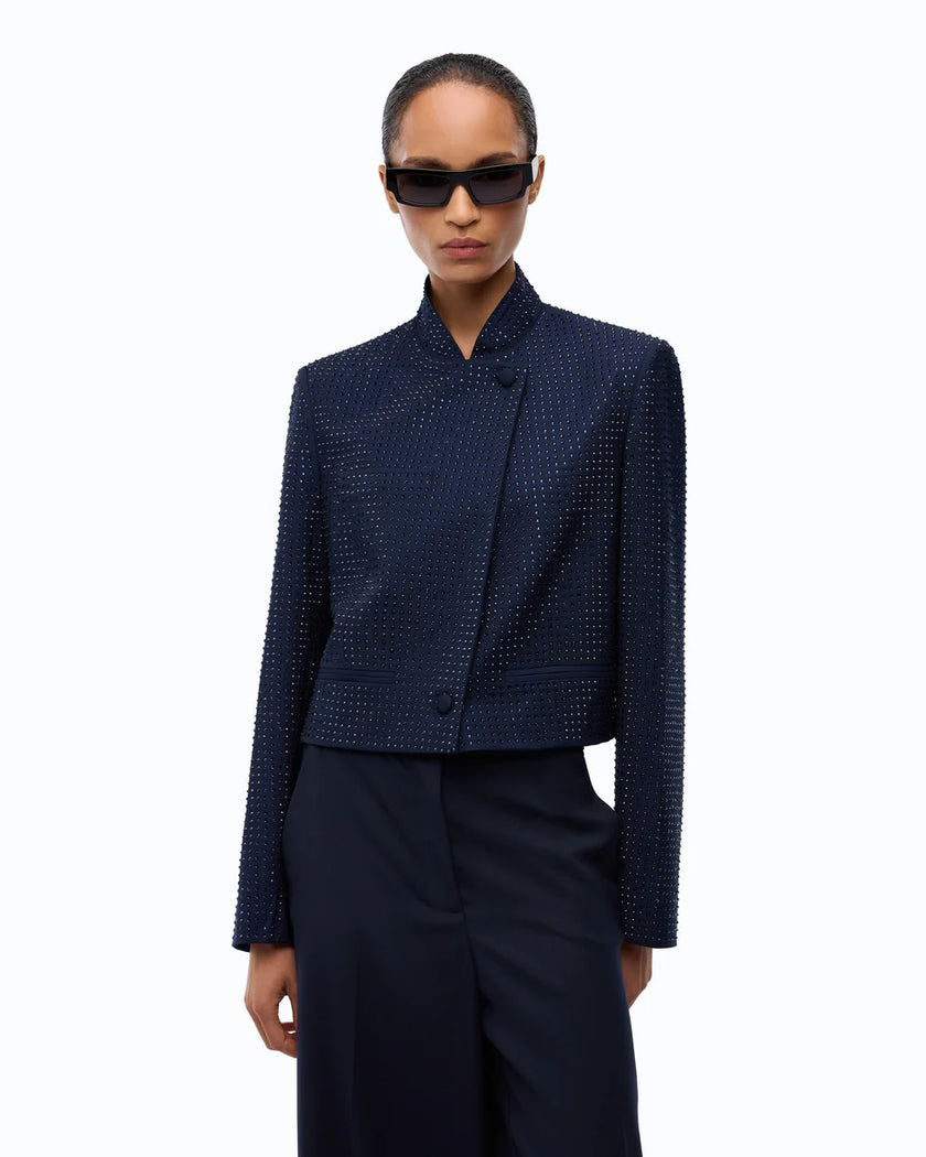 A model wearing a dark navy textured jacket with a high stand collar and a wrap-style front, paired with dark trousers and black sunglasses, against a plain white background.

PINKO Cropped Jacket with Rhinestones. Available at Edit by Elaine Turner in Houston, TX. Close Up model view. 