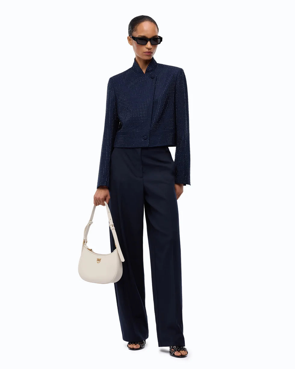 A model stands against a plain white background wearing a dark navy textured jacket and matching wide-leg trousers, holding a cream-colored handbag.

PINKO Cropped Jacket with Rhinestones. Available at Edit by Elaine Turner in Houston, TX. Full front model view. 