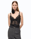 A model wearing a black lace camisole top with a floral ruffle collar detail, paired with dark gray trousers and a black choker necklace, against a plain white background.
Pinko Tiare top jacquard crinkle black. Available at Edit by Elaine Turner in Houston, TX. Model front view. 