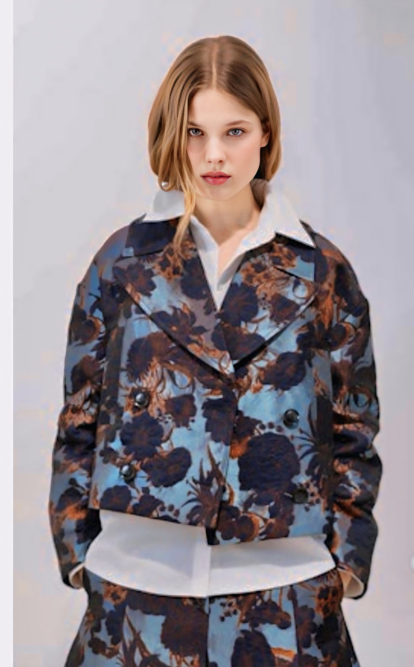 A model wearing a cropped, double-breasted jacket and matching trousers featuring a blue, brown, and black floral pattern over a white collared shirt, set against a plain light gray background.

Psophia - Jacquard Jacket in Steel 

Available at Edit by Elaine Turner in Houston, TX. Full model front view. 