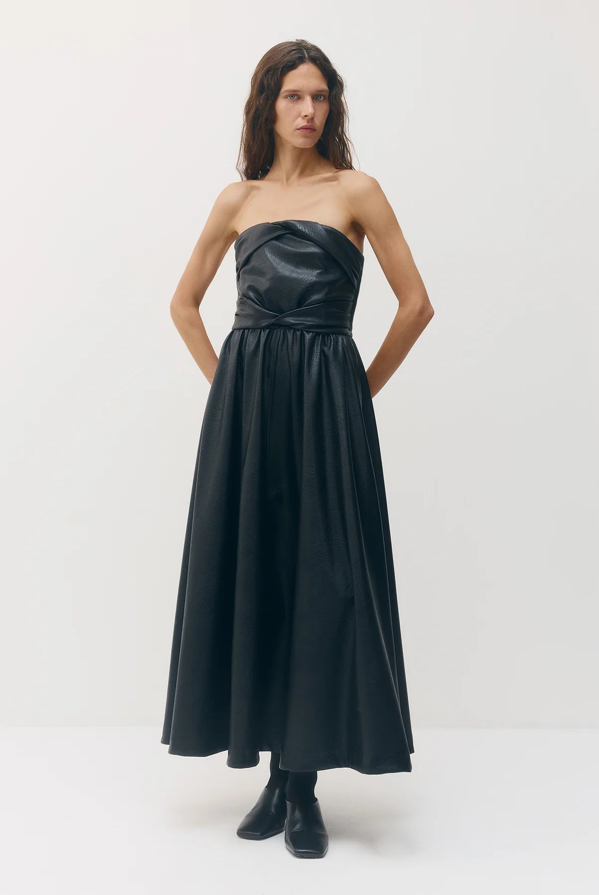 A woman modeling a strapless black faux-leather maxi dress with a gathered bodice and flowing skirt, paired with black ankle boots, against a plain white studio background.

Sabina Musayev Garner Dress in black. Available at Edit by Elaine Turner in Houston, TX. Front Model View. 