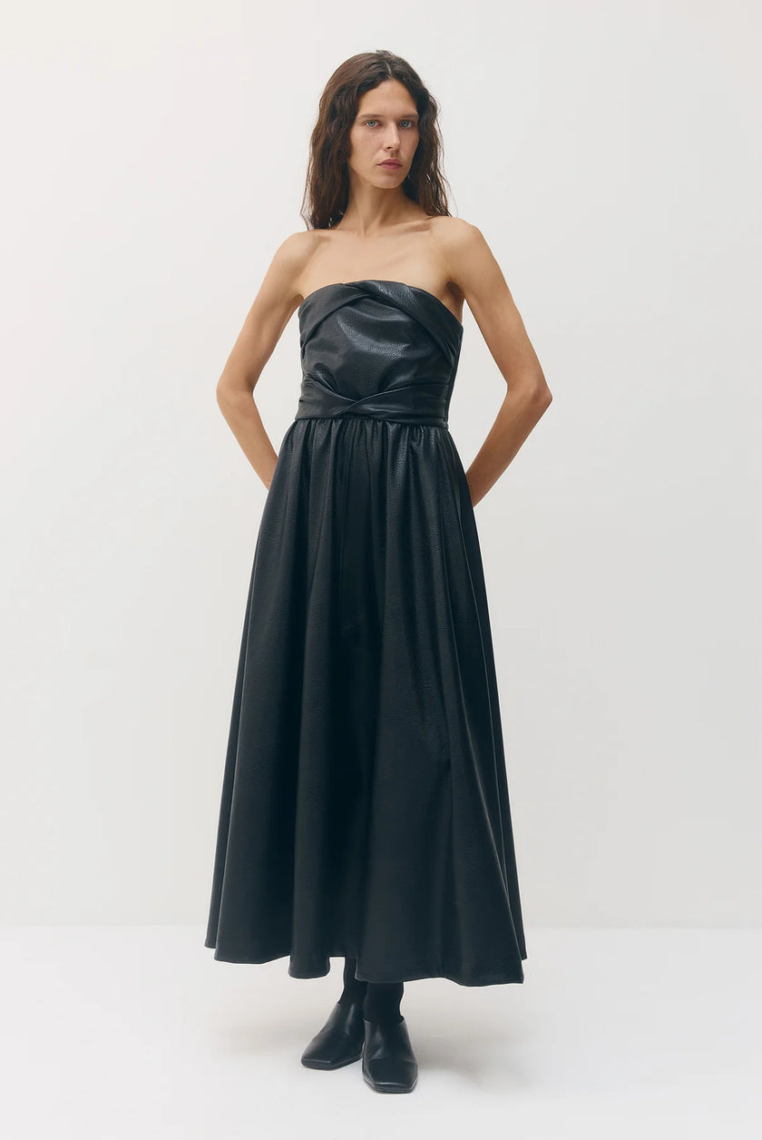 A woman modeling a strapless black faux-leather maxi dress with a gathered bodice and flowing skirt, paired with black ankle boots, against a plain white studio background.

Sabina Musayev Garner Dress in black. Available at Edit by Elaine Turner in Houston, TX. Front Model View. 
