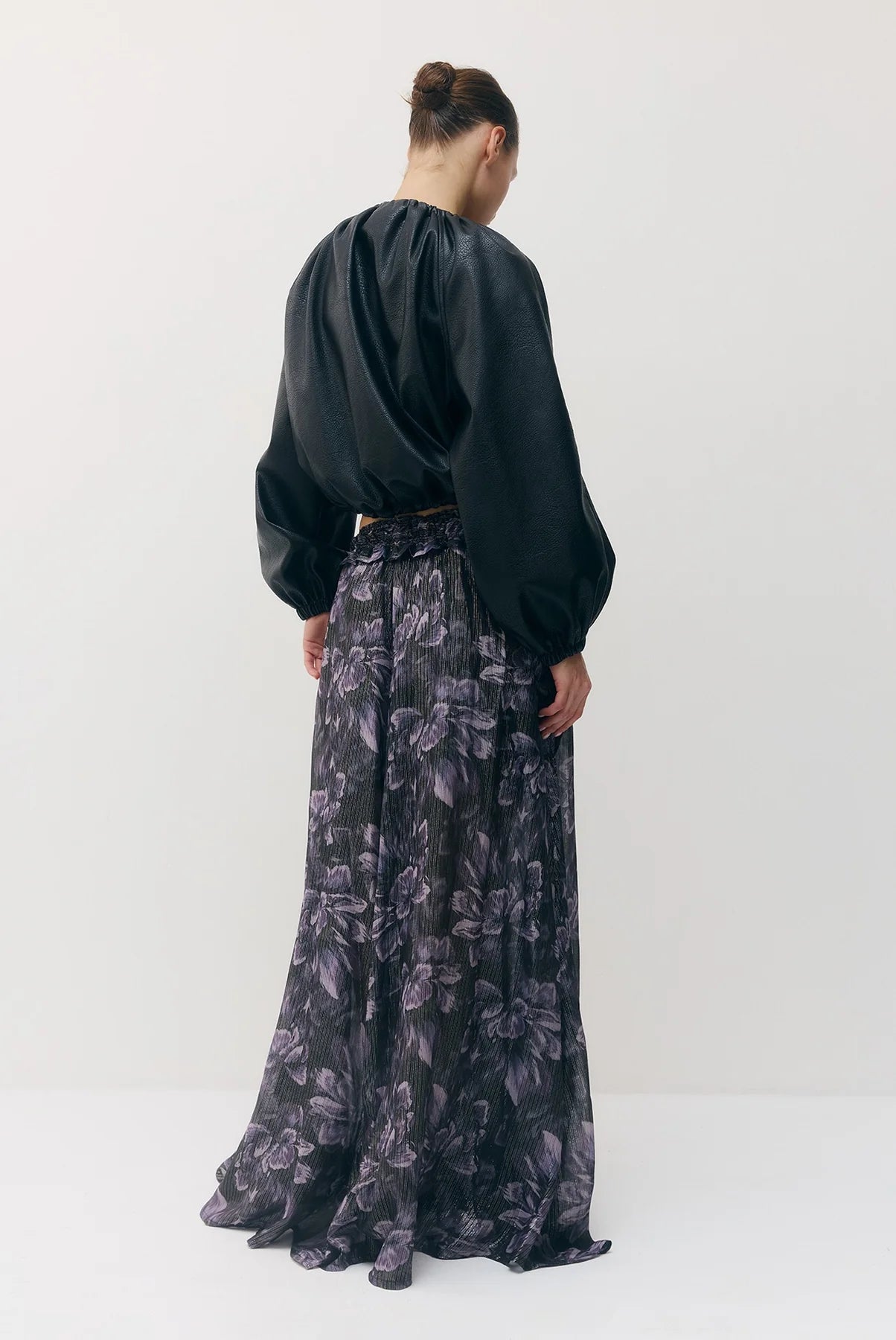 A model shown from the back wearing a black long-sleeve vegan leather jacket and a high-waisted, floor-length black skirt with a dark purple floral pattern, set against a plain white studio background.

Sabina Musayev Tomas Jacket in black. Available at Edit by Elaine Turner in Houston, TX. Back Model View. 