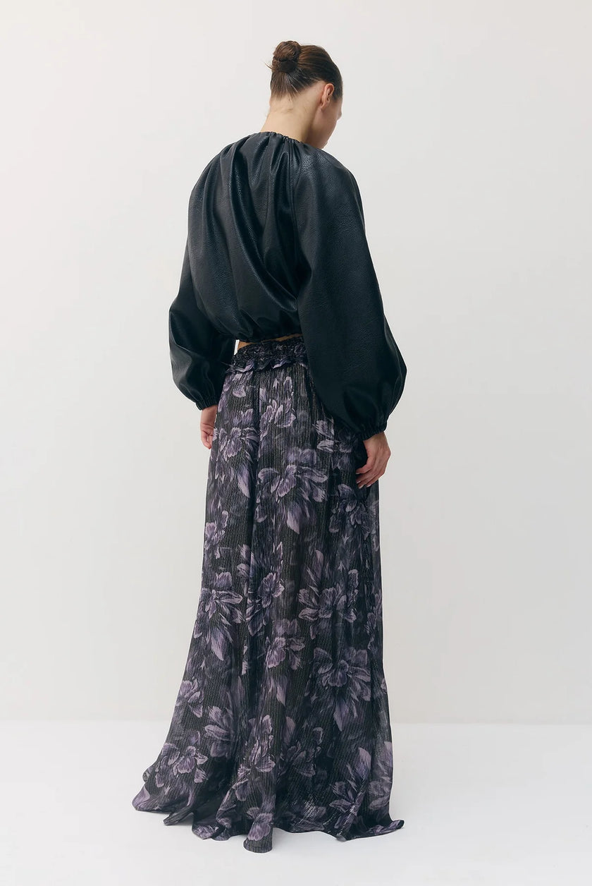 A model shown from the back wearing a black long-sleeve vegan leather jacket and a high-waisted, floor-length black skirt with a dark purple floral pattern, set against a plain white studio background.

Sabina Musayev Tomas Jacket in black. Available at Edit by Elaine Turner in Houston, TX. Back Model View. 