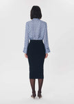 A woman viewed from the back wearing a long-sleeve button-up shirt with a blue and white geometric pattern and a dark navy pencil skirt, paired with sheer black tights and brown heels, against a plain light gray studio background.

Tara Jarmon- Jeannette Knit Skirt in Nuit. Available at Edit by Elaine Turner in Houston, TX. Back Model View. 