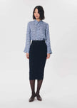 A woman stands against a plain light gray studio background wearing a long-sleeve button-up shirt with a blue and white geometric pattern, paired with a dark navy pencil skirt, dark tights, and dark brown shoes.

Tara Jarmon- Jeannette Knit Skirt in Nuit. Available at Edit by Elaine Turner in Houston, TX. Front Model View. 