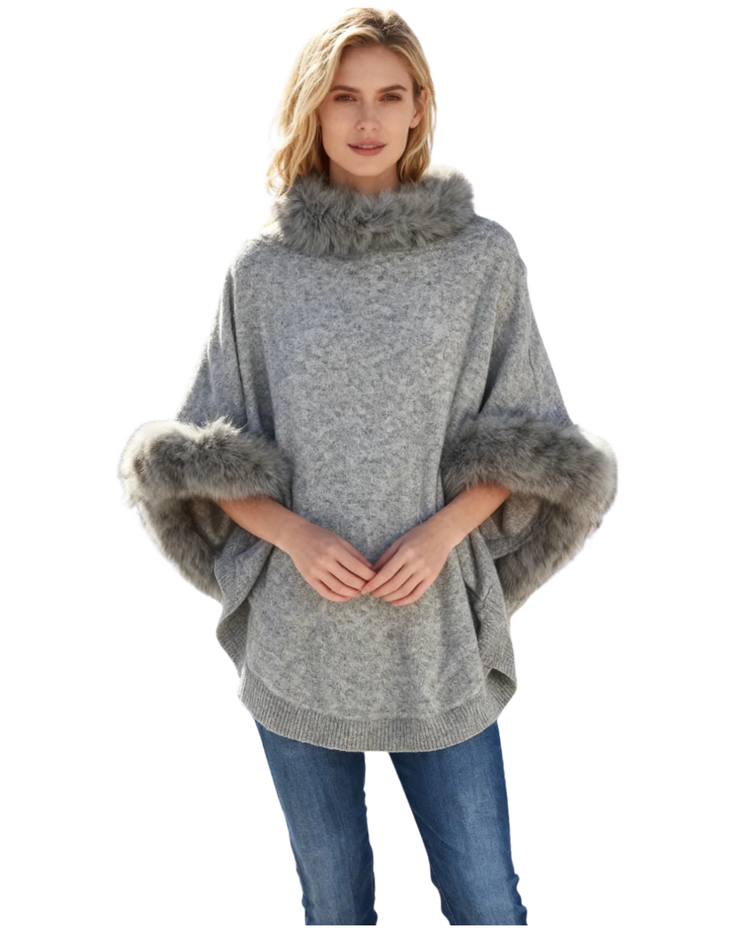 Woman wearing a gray poncho by Cortland Park with  faux fur trim on a white background at edit. BY ELAINE TURNER.
